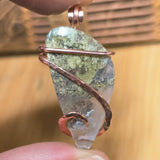 Pendant with green stone and copper wire wrapping held by a hand against a blurred background