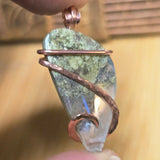 Jewelry pendant with green stone and copper wire wrapping on a blurred background