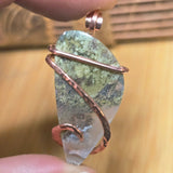 Pendant with green stone and copper wire wrapping held by a hand against a blurred background
