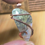 Jewelry with a stone and copper wire wrapping held by a hand against a blurred background