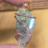 Jewelry pendant with copper wire wrapping held between fingers against a blurred background