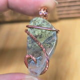 Pendant with natural stone and copper wire wrapping held between fingers against a blurred background