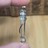 Clear crystal pendant wrapped in copper held between fingers against wooden background.  