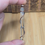 Water Clear Quartz Crystal wrapped in copper held in front of blurred wood background 