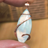 Marquis-shaped pendant with copper wire wrapping held between fingers against a blurred background