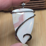 White stone pendant with silver and black wire wrapping held by a hand on a wooden surface