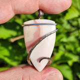 Hand holding a pink and white swirl pendant with a blurred green background