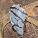 Copper wire wrapped around a piece of white crystal on a textured brown background