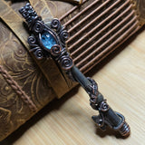 Antique skeleton key wire wrap pendant with aquamarine accent against a leather book on a wood surface