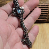 Antique skeleton key wire wrap pendant with aquamarine accent against a leather book on a wood surface