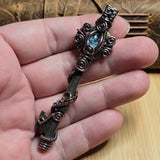 Antique skeleton key wire wrap pendant with aquamarine accent against a leather book on a wood surface