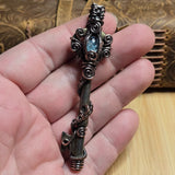 Antique skeleton key wire wrap pendant with aquamarine accent against a leather book on a wood surface