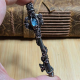 Antique skeleton key wire wrap pendant with aquamarine accent against a leather book on a wood surface