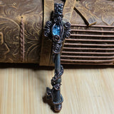 Antique skeleton key wire wrap pendant with aquamarine accent against a leather book on a wood surface