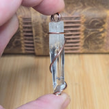 Water Clear Quartz Crystal wrapped in copper held in front of blurred wood background 