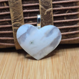 Heart-shaped silver pendant on a wooden surface with a brown textured background